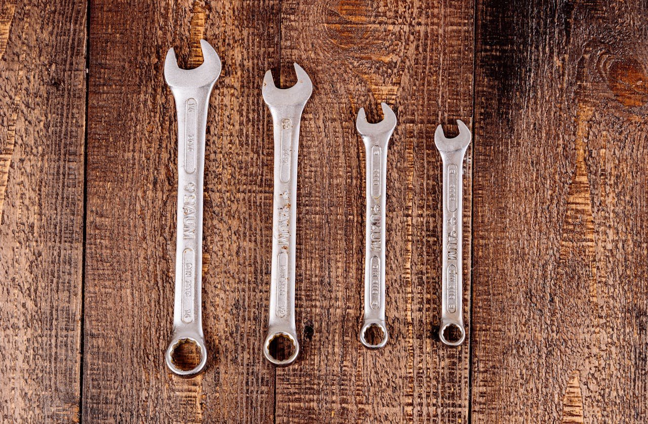 Flat lay of four metal wrenches on a rustic wooden surface, ideal for workshop or DIY themes.